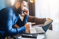 Young bearded businessman is sitting at table in front of computer,talking on cell phone,showing finger on laptop screen Royalty Free Stock Photo