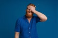 Young smiling bearded man covering his face with hand isolated over blue background Royalty Free Stock Photo