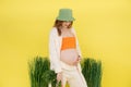 Young smiling beauteous pregnant woman wear green bucket hat, orange top, beige cardigan holding bunch of fresh carrots. Royalty Free Stock Photo