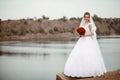 A young smiling and beautiful bride in a white dress is standing against a background of rocks, cliffs and stones.