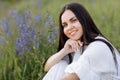 Young smiling beautiful brunette woman in white dress is sitting in green meadow with lupine flowers in spring Royalty Free Stock Photo