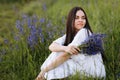Young smiling beautiful brunette woman in white dress is sitting in green meadow with lupine flowers in spring Royalty Free Stock Photo