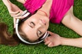 Young smiling beautiful girl laying on the grass in park listeni