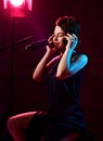 Young beautiful short haired brunette woman singer in black dress sitting in studio in headphones and listening to music