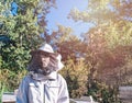 Young smiling beekeeper with mask and bee sting protection suit while observing the beehives in the middle of the bush