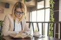 Young smiling blonde woman in a restaurant reading a book and drinking coffee Royalty Free Stock Photo