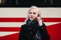 Young smiling blonde woman talking on the phone on the background of the tram. Outdoor portrait of a girl.