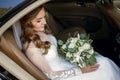 A young smiling bride sits in a car and holds a white wedding bouquet of roses in her hands Royalty Free Stock Photo