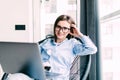 Young smiling brunette girl is sitting on modern chair near the window in light cozy room at home working on laptop in relaxing Royalty Free Stock Photo