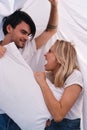 Young smiling brunette man and pretty emotional blond woman happily looking at each other and fighting for pillow lying Royalty Free Stock Photo