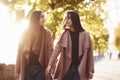 Young smiling brunette twin girls looking at each other, holding hands in casual coat and walking at autumn sunny park Royalty Free Stock Photo