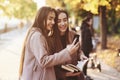 Young smiling brunette twin girls looking at each other and taking selfie with black phone, while one of them is holding Royalty Free Stock Photo