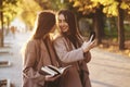 Young smiling brunette twin girls looking at each other and taking selfie with black phone, while one of them is holding Royalty Free Stock Photo