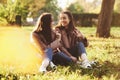 Young smiling brunette twin girls sitting on grass with legs crossed and slightly bent in knees wearing casual coat Royalty Free Stock Photo