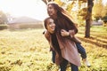 Young smiling brunette twin sisters having fun and doing a piggy back riding in autumn sunny park on blurry background Royalty Free Stock Photo