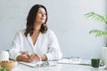 Young smiling brunette woman nutritionist plus size in white shirt working at laptop on table with house plant in bright modern