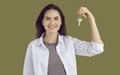 Young smiling brunette woman in a white shirt is holding key in hand on khaki background. Royalty Free Stock Photo