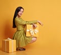 Young smiling brunette woman in yellow suit skirt, short jacket and high-heeled shoes sits sideways holding gift box Royalty Free Stock Photo