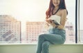 Young smiling business asian woman sitting near window and uses digital tablet Royalty Free Stock Photo