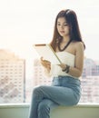 Young smiling business asian woman sitting near window and uses digital tablet Royalty Free Stock Photo