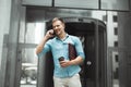 Young smiling business man with cup of coffee and laptop in his hands talking on the phone standing near entrance to Royalty Free Stock Photo