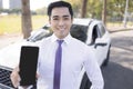 Young smiling business man showing mobile phone with black empty screen and standing before the car Royalty Free Stock Photo