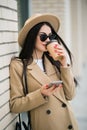 Young smiling business woman in sunglasses and coat stands near office centre with cup of coffee and talks on smart phone. Royalty Free Stock Photo