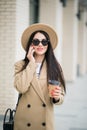 Young smiling business woman in sunglasses and coat stands near office centre with cup of coffee and talks on smart phone. Royalty Free Stock Photo