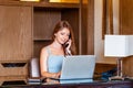 Young smiling business woman using laptop computer, calling by phone in modern apartment. Attractive businesswoman Royalty Free Stock Photo