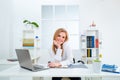 Young smiling business woman in white modern office. Beauty secretary. Beautiful young woman working with laptop in