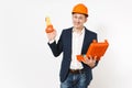 Young smiling businessman in dark suit, protective construction orange helmet holding opened case with instruments or