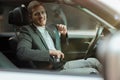 Young smiling businessman sitts in his car looks happy and satisfied, adjusting his safety belt before starting his trip, safety Royalty Free Stock Photo