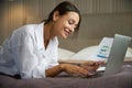 Young smiling businesswoman with documents typing on laptop on bed in hotel room Royalty Free Stock Photo