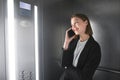 Young smiling businesswoman is talking by her smartphone in the elevator. Female office worker laughing and talking by phone in Royalty Free Stock Photo