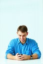 Young smiling casual businessman sitting at the table and looking at smartphone Royalty Free Stock Photo