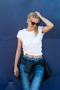 Young smiling casual woman with sunglasses white t shirt and jeans against blue metal door in city summer day