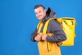 Young smiling caucasian food delivery guy in yellow uniform and refrigerator bag on his back waves finger up in approval
