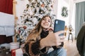 Young smiling caucasian woman making selfie using mobile phone near Christmas tree at home Royalty Free Stock Photo