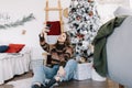 Young smiling caucasian woman making selfie using mobile phone near Christmas tree at home Royalty Free Stock Photo