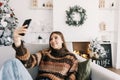 Young smiling caucasian woman making selfie using mobile phone near Christmas tree at home Royalty Free Stock Photo