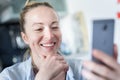 Young smiling cheerful pleased woman indoors at home kitchen using social media apps on mobile phone for chatting and Royalty Free Stock Photo