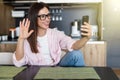 Young smiling cheerful woman at home kitchen using social media apps on phone for video chatting and stying connected with her Royalty Free Stock Photo