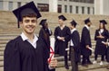 Young smiling confident man student in a university graduate gown and diploma in hands.