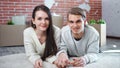 Young smiling couple holding hands lying on floor posing looking at camera medium close-up