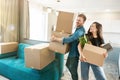 Young smiling couple husband and wife looking happy standing with boxes in their hands in new appartment unpacking boxes