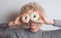 Young smiling curly woman with two donuts near face Royalty Free Stock Photo