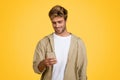 Young smiling European man texting on cellphone, standing on yellow background