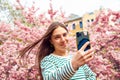 Young smiling european white female student taking selfie portrait with mobile phone. Making selfie woman on smartphone on cherry Royalty Free Stock Photo