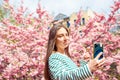 Young smiling european white female student taking selfie portrait with mobile phone. Making selfie woman on smartphone on cherry Royalty Free Stock Photo