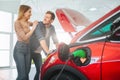 Young smiling family buying first electric car in the showroom. Attractive couple are enjoy to buy an eco-friendly car Royalty Free Stock Photo